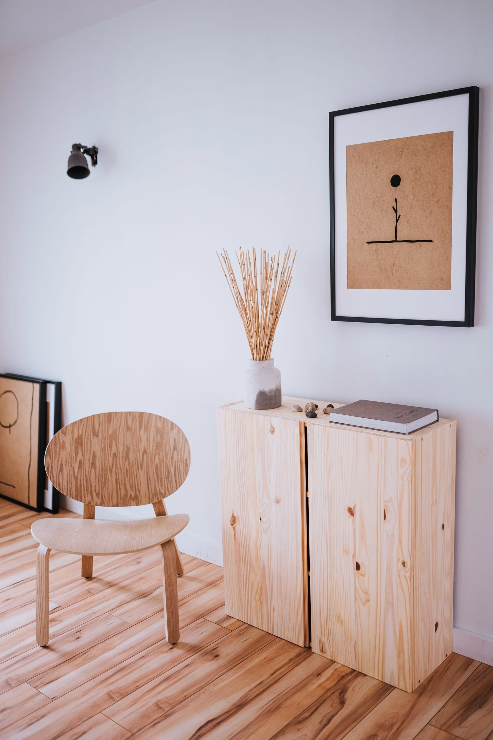 A styled vignette of a framed print, dried grasses and a pale timber cabinet