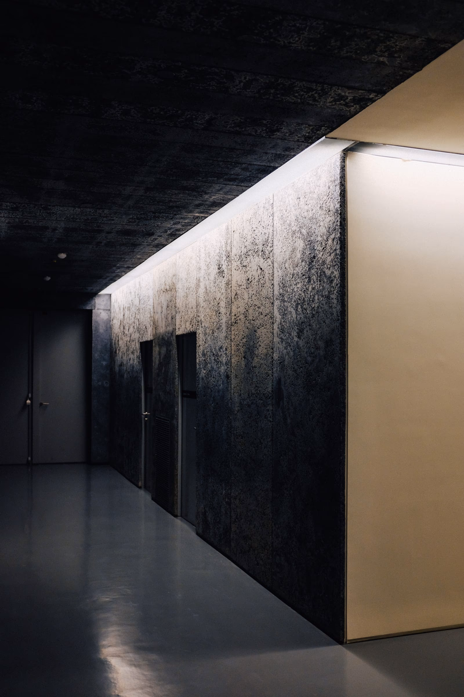 The approach corridor in neutral plaster, kept dark so the shooting floor reads bright