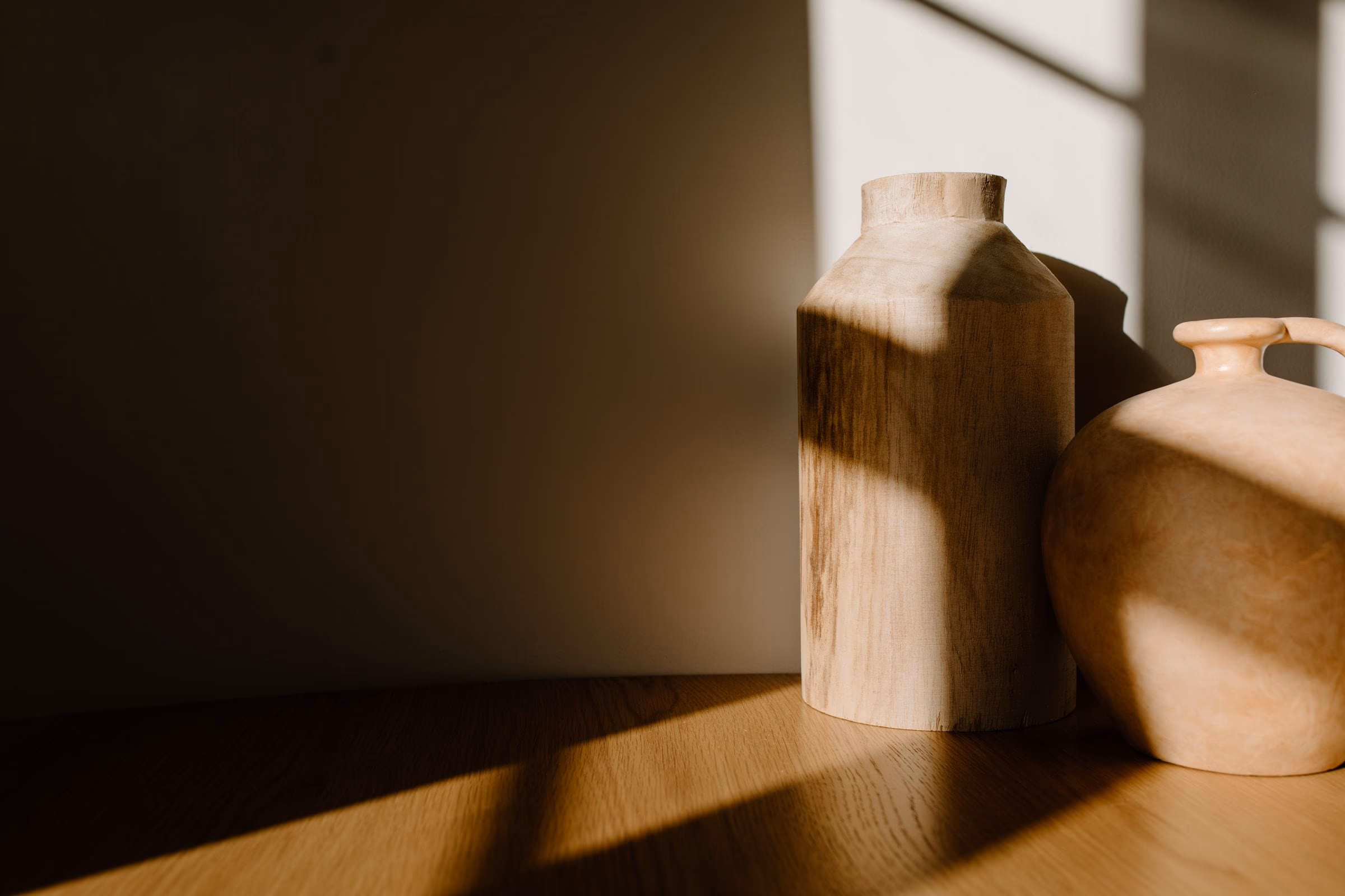 Late sunlight raking across two turned timber vessels and the wall behind them